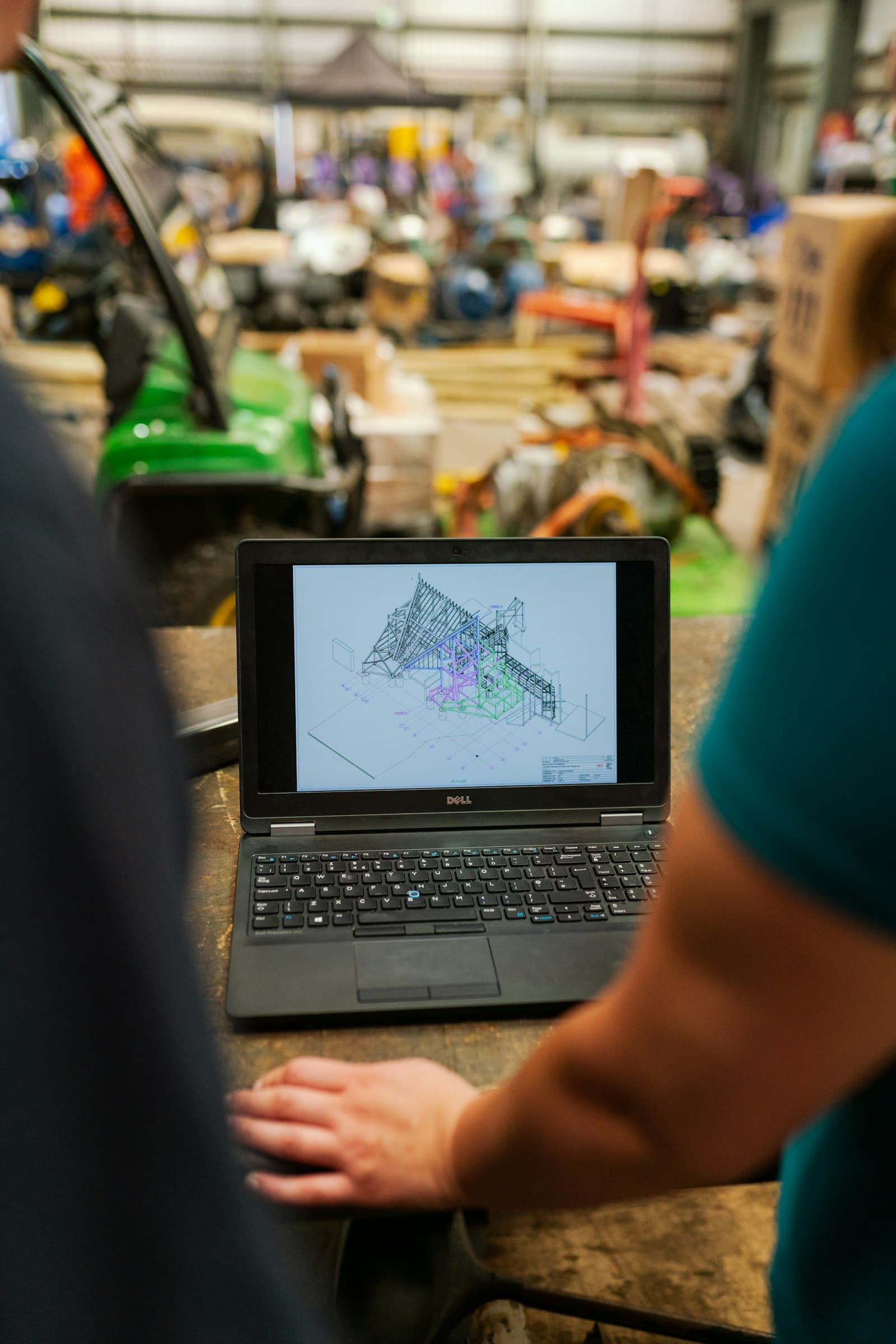 A laptop showing a 3D model of a steel structure, on a workshop bench